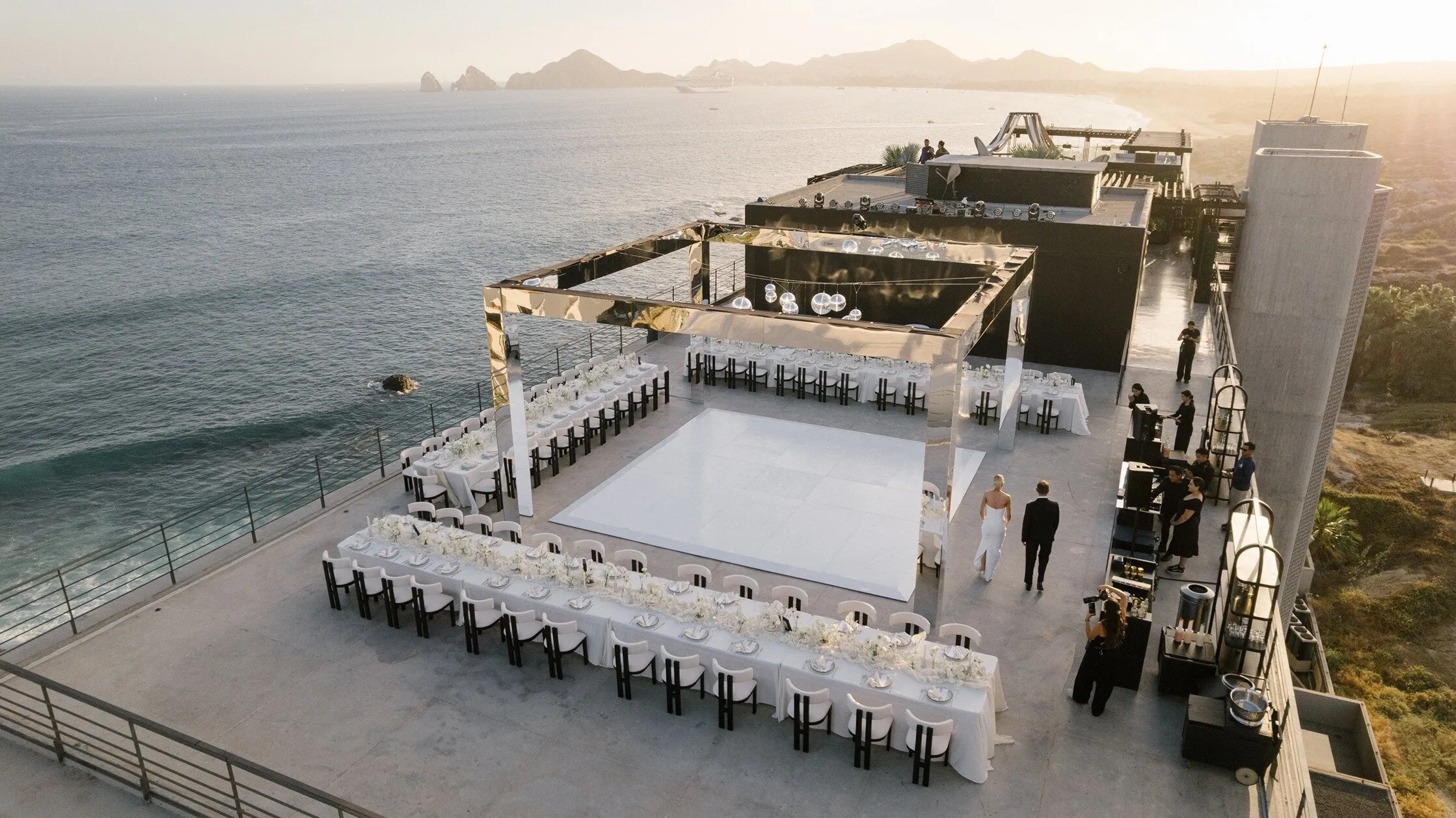 A clifftop reception laid out above the Pacific at dusk, the Arch of Cabo San Lucas on the horizon