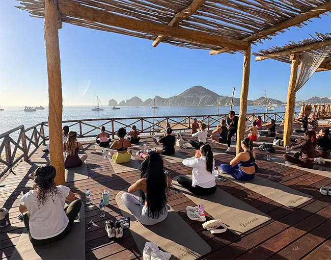 A class under a palapa, the Arch and the bay of Cabo San Lucas beyond
