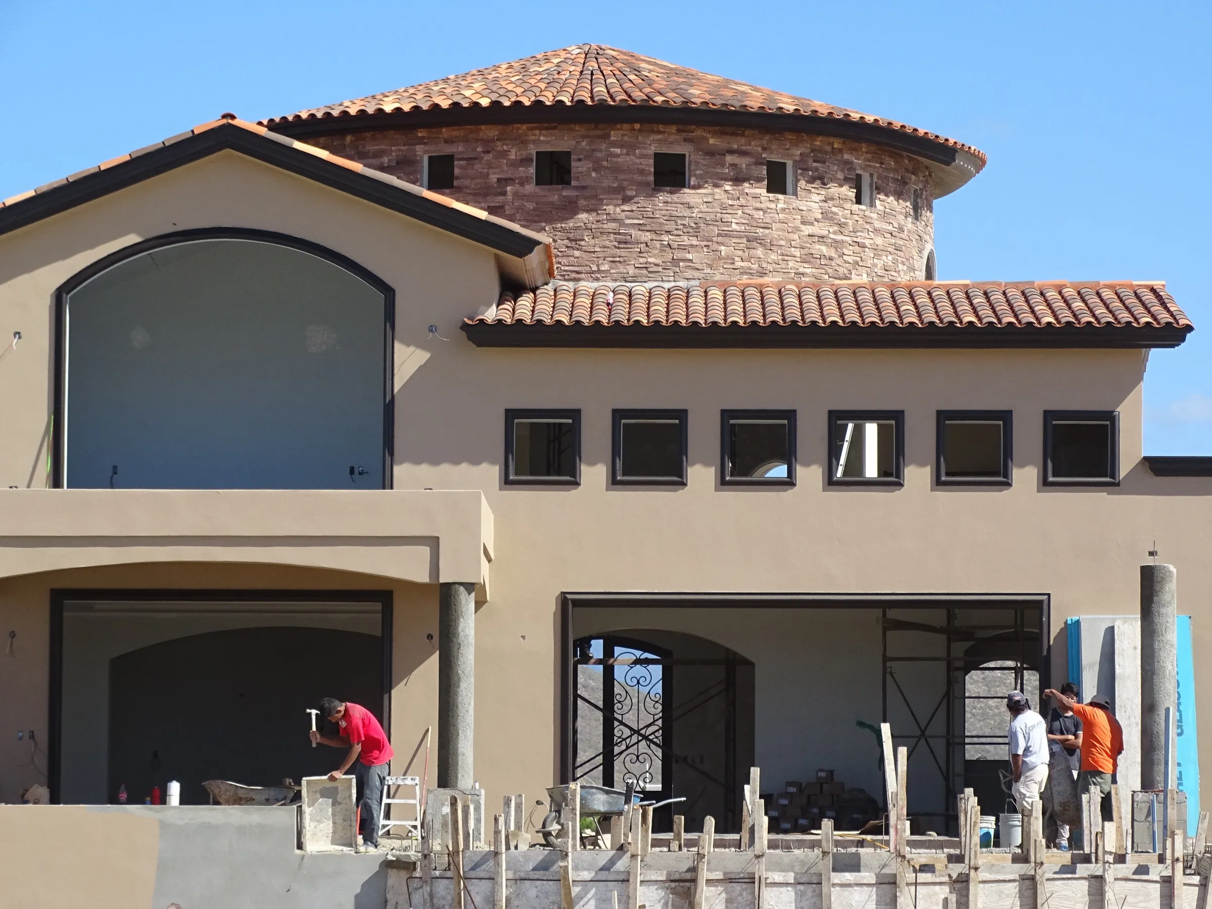 Masons at work on a half-built house near Todos Santos, its tiled roof and stone turret already up