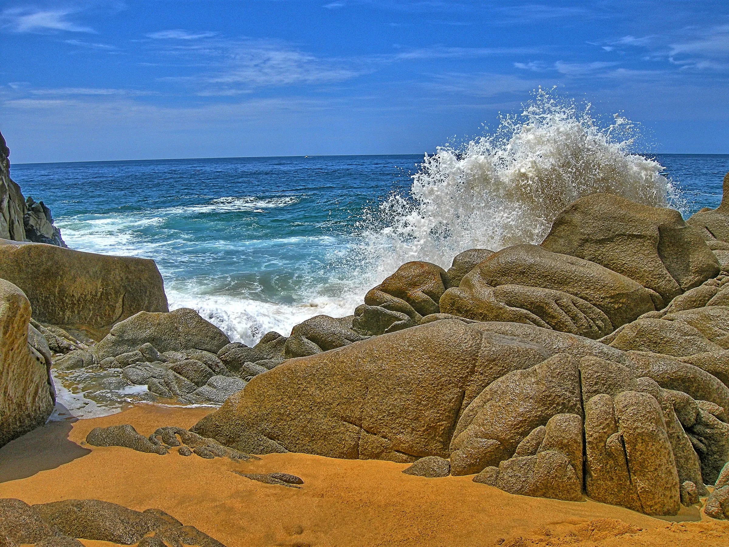 A wave breaking over granite boulders at a sand cove near Land’s End