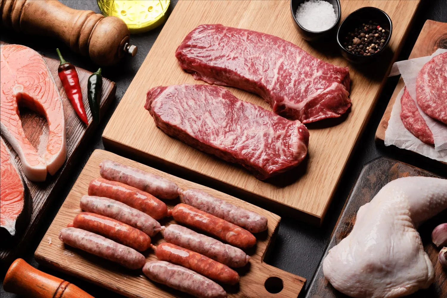 A board of cuts — steak, sausage, chicken and salmon — laid out with oil, salt and pepper
